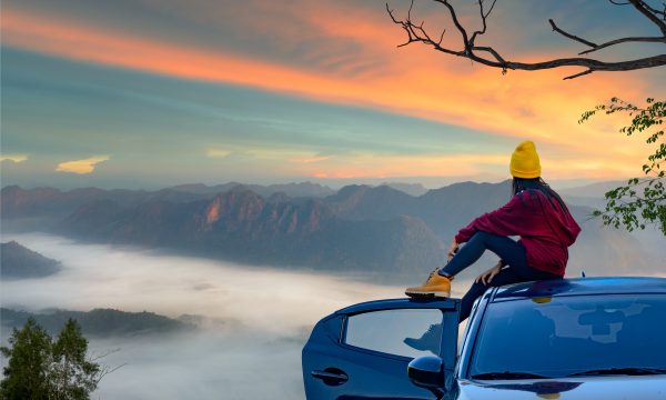 Woman sitting on car looking at mountains