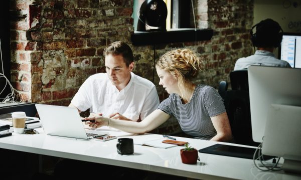 Man and woman look at laptop screen together at desk