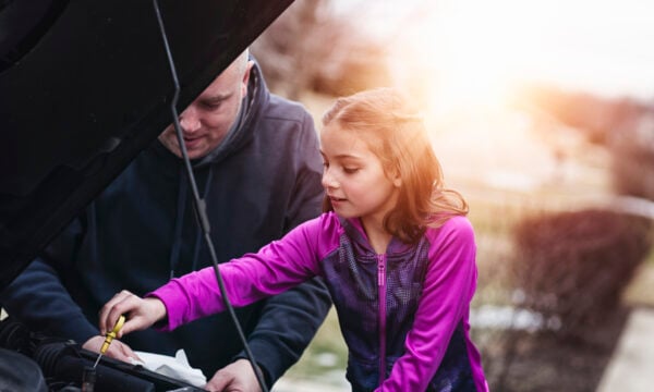 father and daughter checking oil in car
