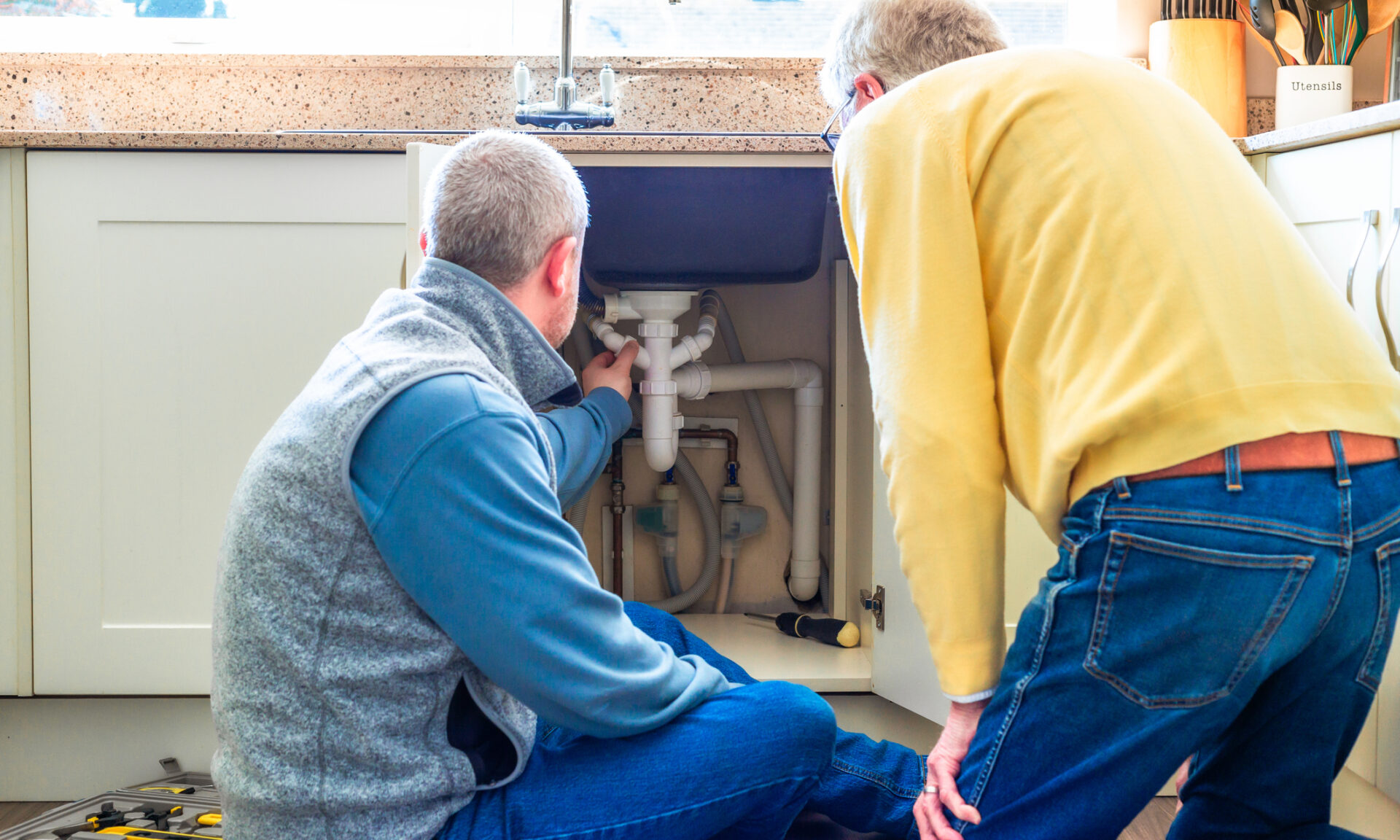 Two people looking at pipes under a sink.