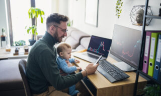 Person with baby looking at financial performance on computer in home office.