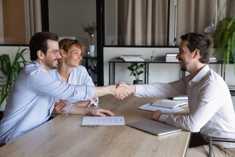 A confident bank associate meeting and shaking hands with happy couple.