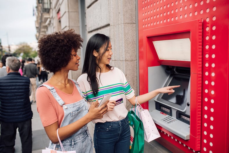 Two girls smile as they take the money from the ATM for shopping.