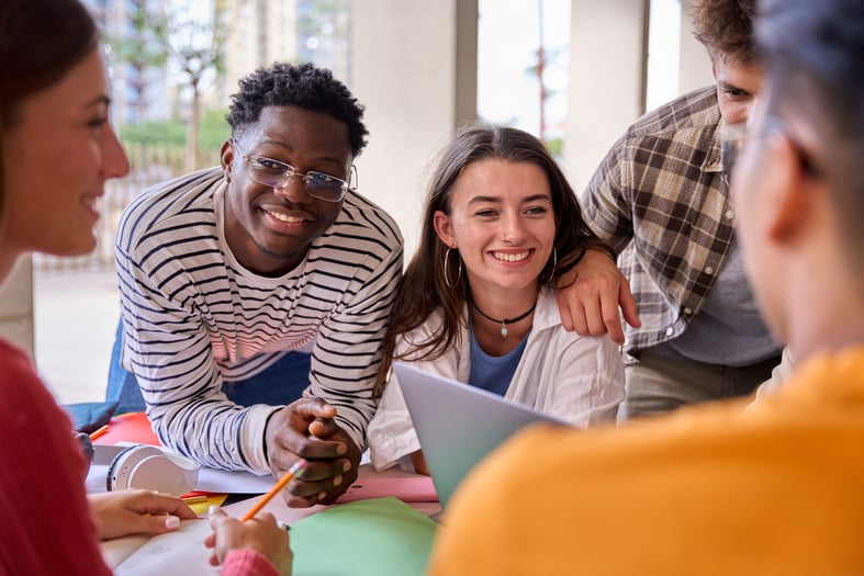 Cheerful multiracial group of young students working together with their classmates on a project sitting at a table in the faculty.