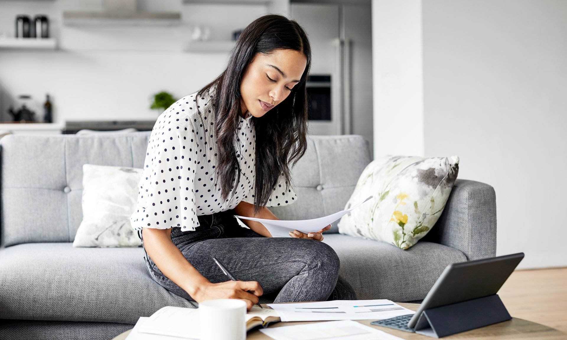 A woman sitting in a living room with papers and a tablet — an image of what learning how to invest money can look like.