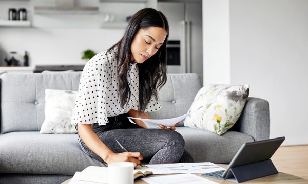 A woman sitting in a living room with papers and a tablet — an image of what learning how to invest money can look like.