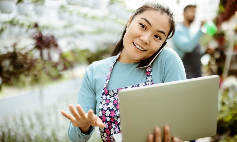 Asian Woman Working at the Plants Nursery Using Smartphone and Laptop