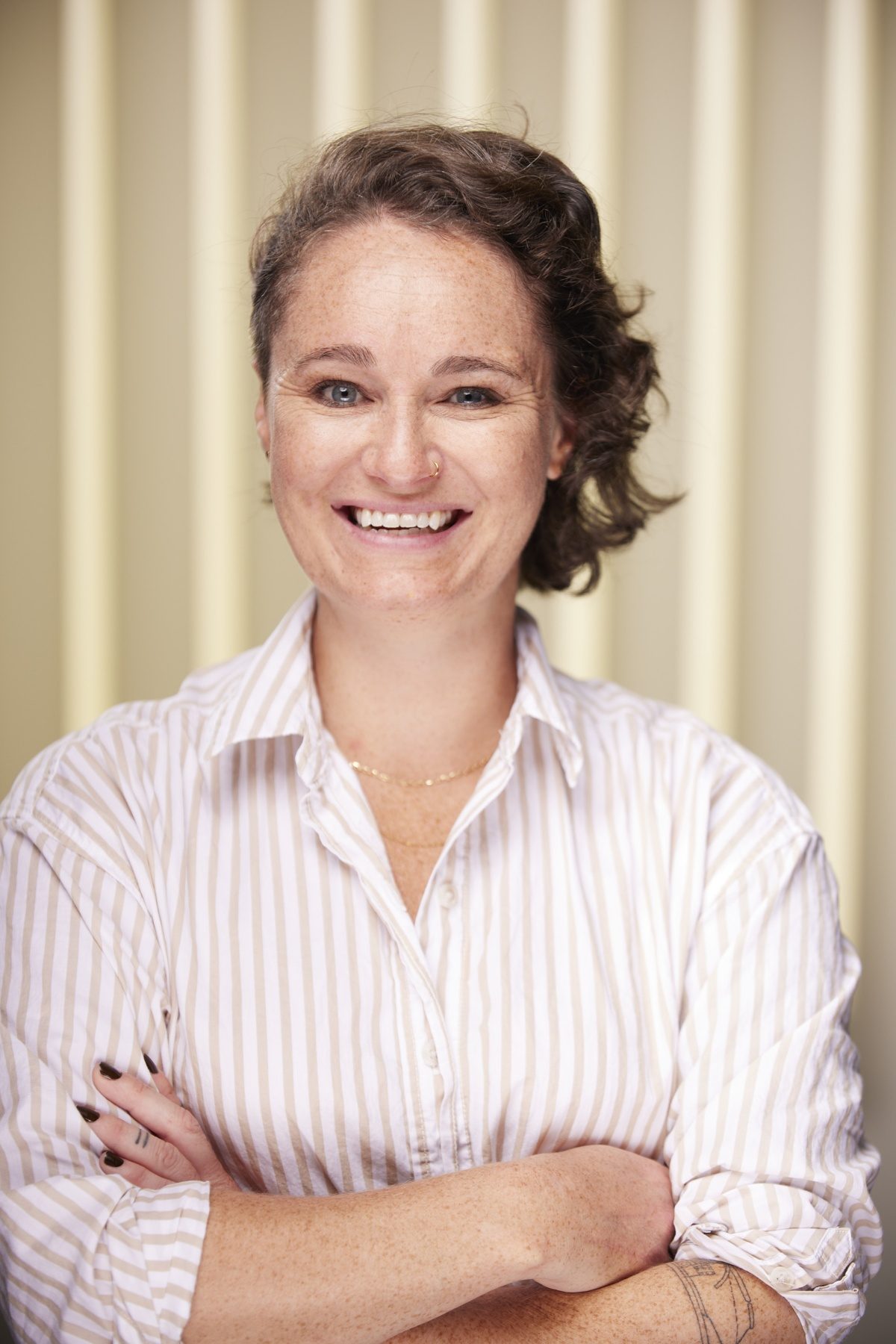 Woman business owner with short hair wears striped shirt, crosses arms and smiles at camera